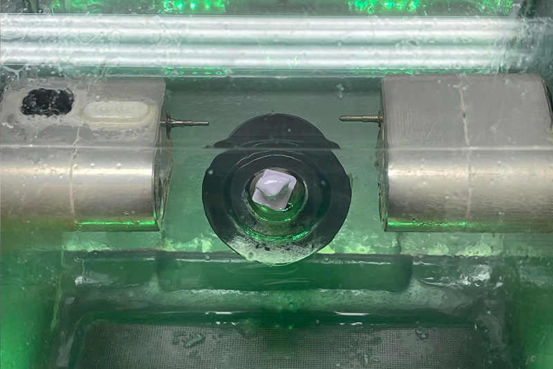 The image shows a close-up of industrial equipment with metallic components, likely in a manufacturing or laboratory setting.