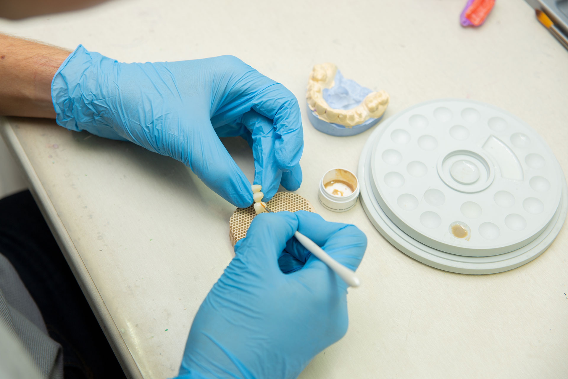 A person in a lab coat is examining a circular object with a magnifying glass, wearing blue gloves and working at a table.