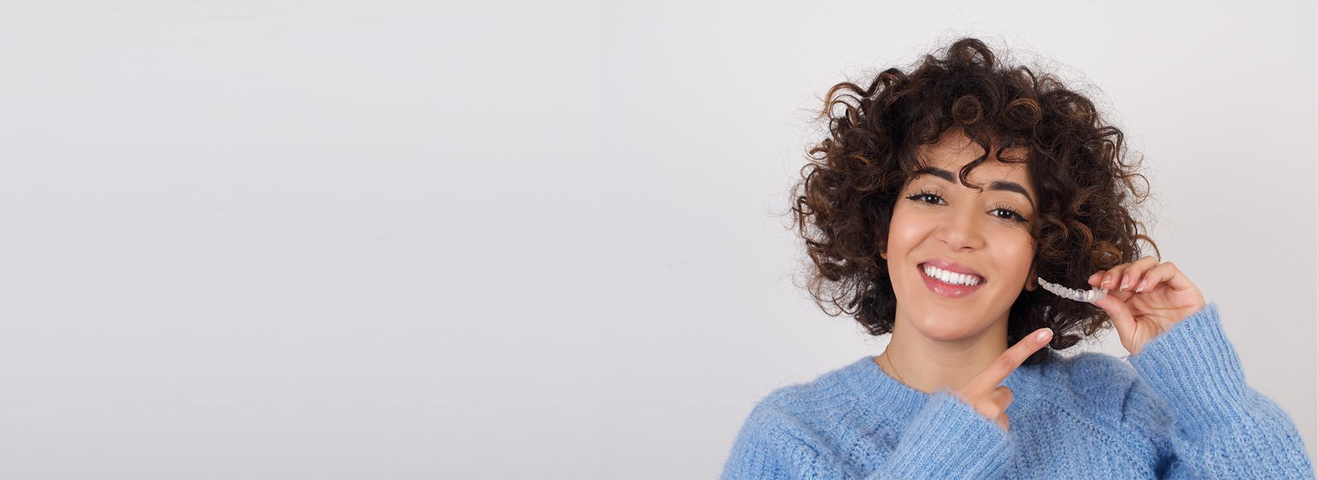 A smiling woman with curly hair, wearing a blue sweater, and holding a phone to her ear.