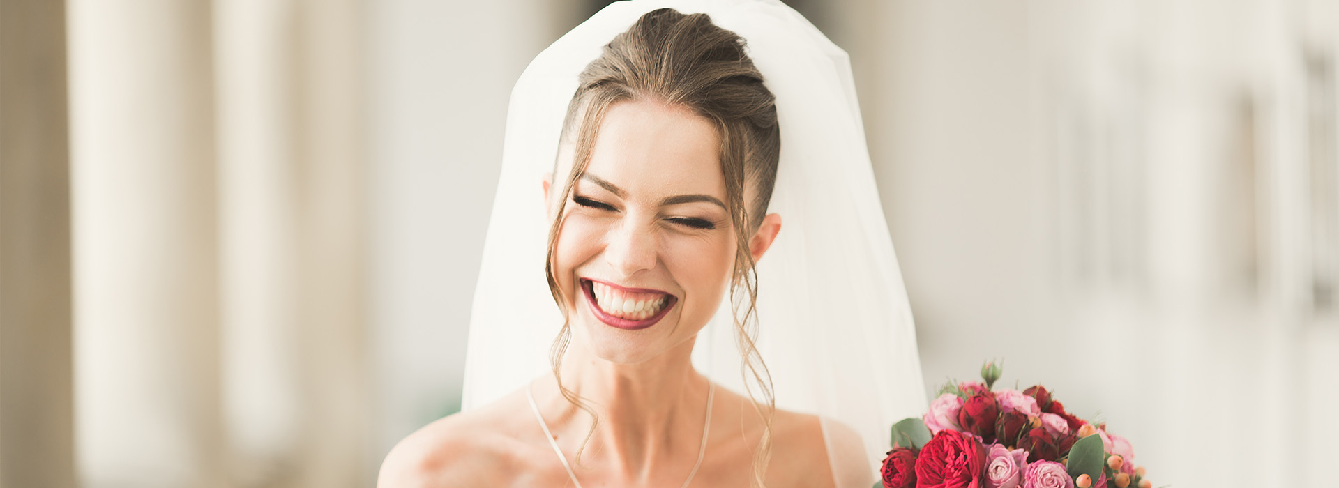A woman wearing a white wedding dress and holding a bouquet, smiling at the camera.
