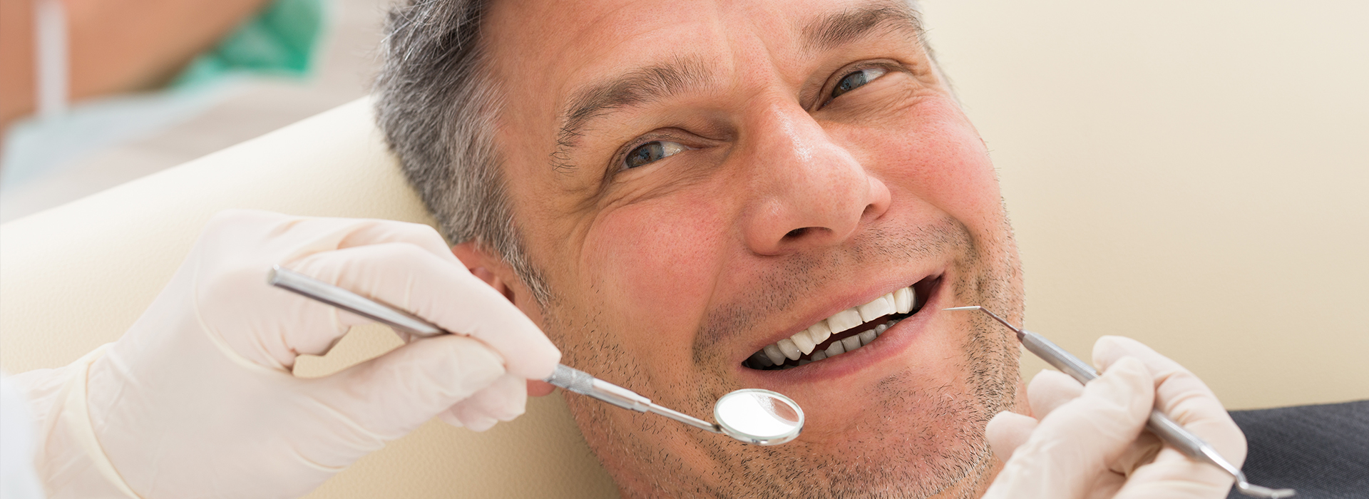 The image shows a man in a dental chair receiving dental care, with a dentist performing a procedure and the patient smiling.