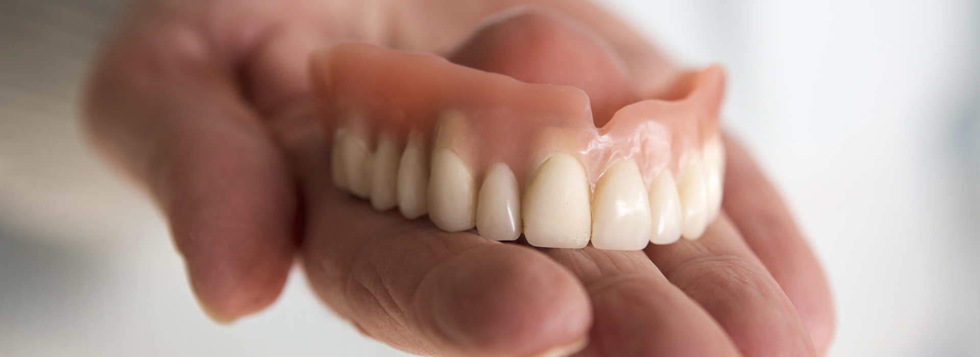 An adult hand holding a set of dentures.