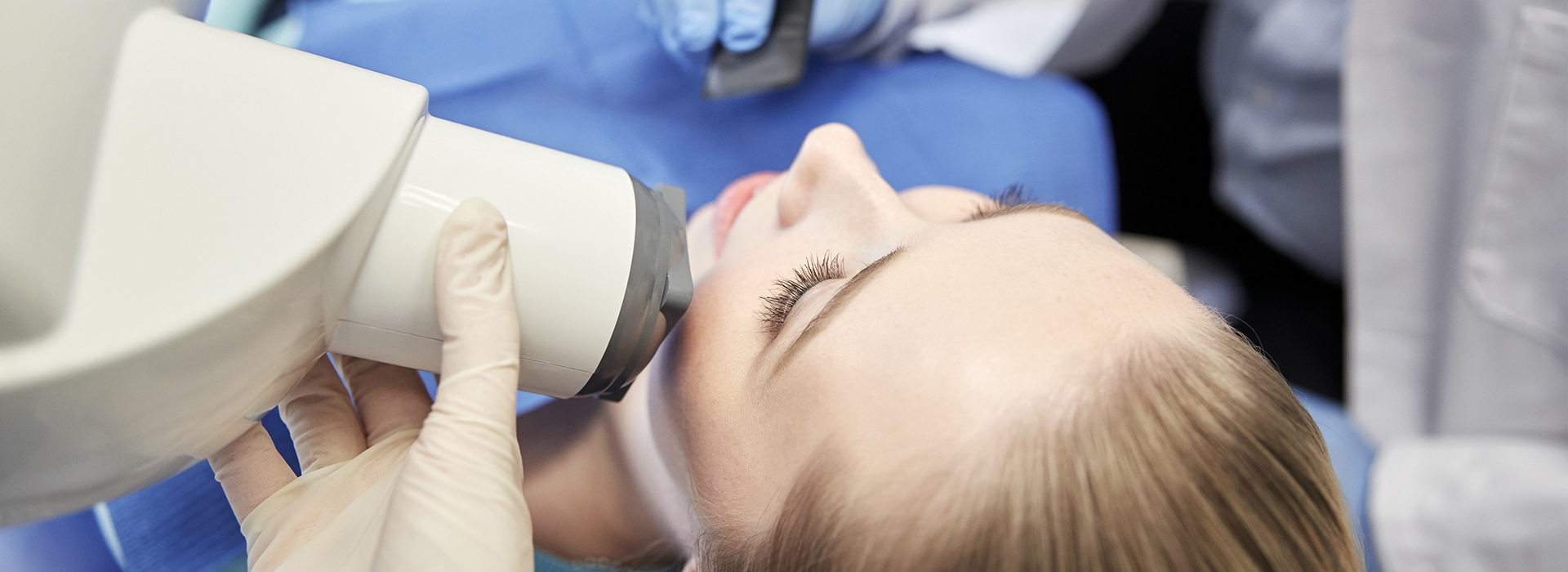 A person receiving a dental examination with a digital X-ray machine and a dental professional in a clinical setting.