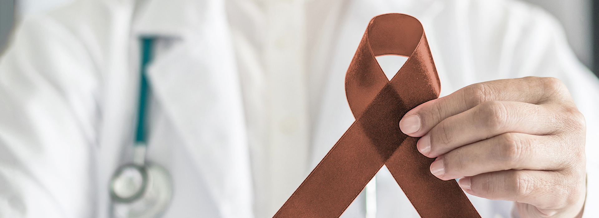 A person in a medical coat holding a tie with a red ribbon, symbolizing awareness for a health condition.