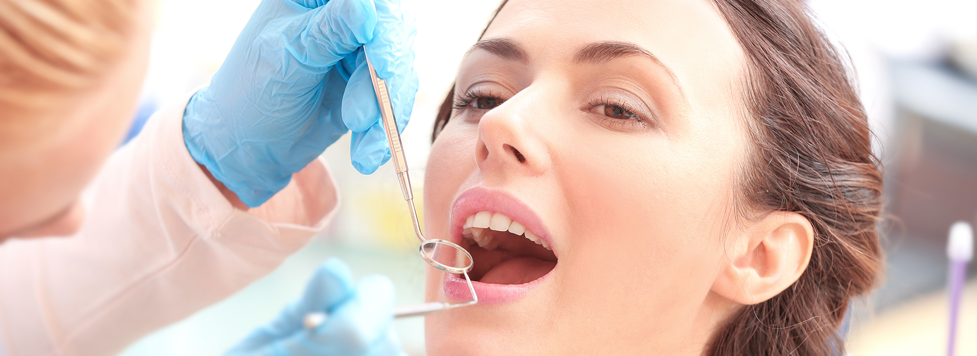 The image shows a woman receiving dental treatment, with a dentist using a drill on her teeth while she is seated in a dental chair.