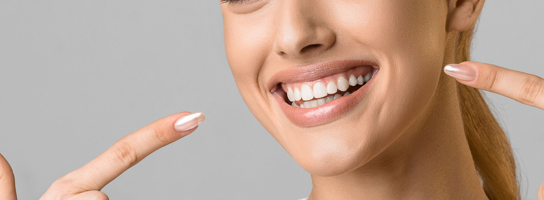 The image shows a woman smiling and pointing at her teeth, with a blurred background.