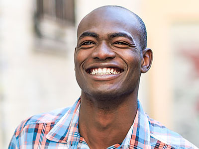 The image is a portrait of a smiling man with short hair, wearing a plaid shirt.