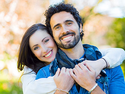 A man and a woman are embracing each other in a joyful pose, both smiling.