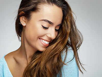 A woman with long brown hair and a radiant smile, looking away from the camera.