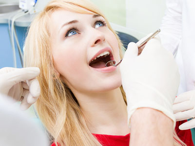Woman receiving dental care, with a dentist performing a procedure and the woman wearing a surgical mask.
