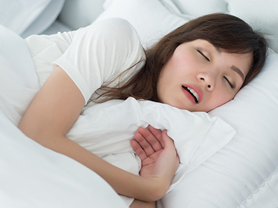 A woman lying in bed with her eyes closed, appearing to be asleep or resting.