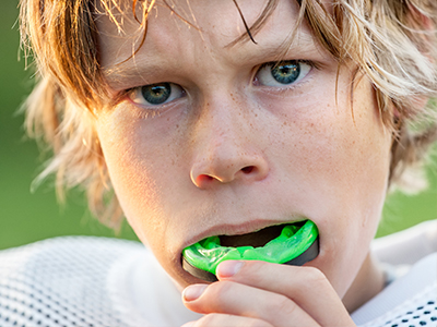 A young boy with a disgruntled expression, holding a green toothbrush to his mouth.