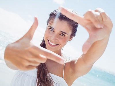 A woman is smiling at the camera, holding up a peace sign with one hand and pointing with the other.