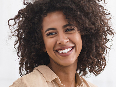 The image is a close-up portrait of a smiling woman with wavy hair, wearing a light brown top.