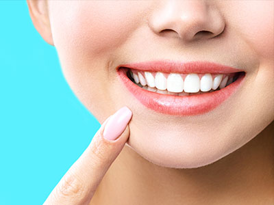 A smiling woman with a toothy grin, showcasing her teeth and lips, against a blue background.